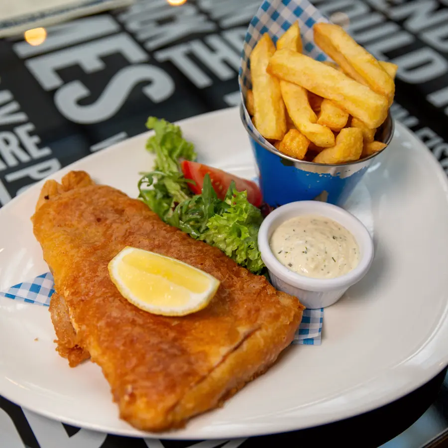 Battered fish and chips with lemon and tartare on a table printed with newspaper headlines